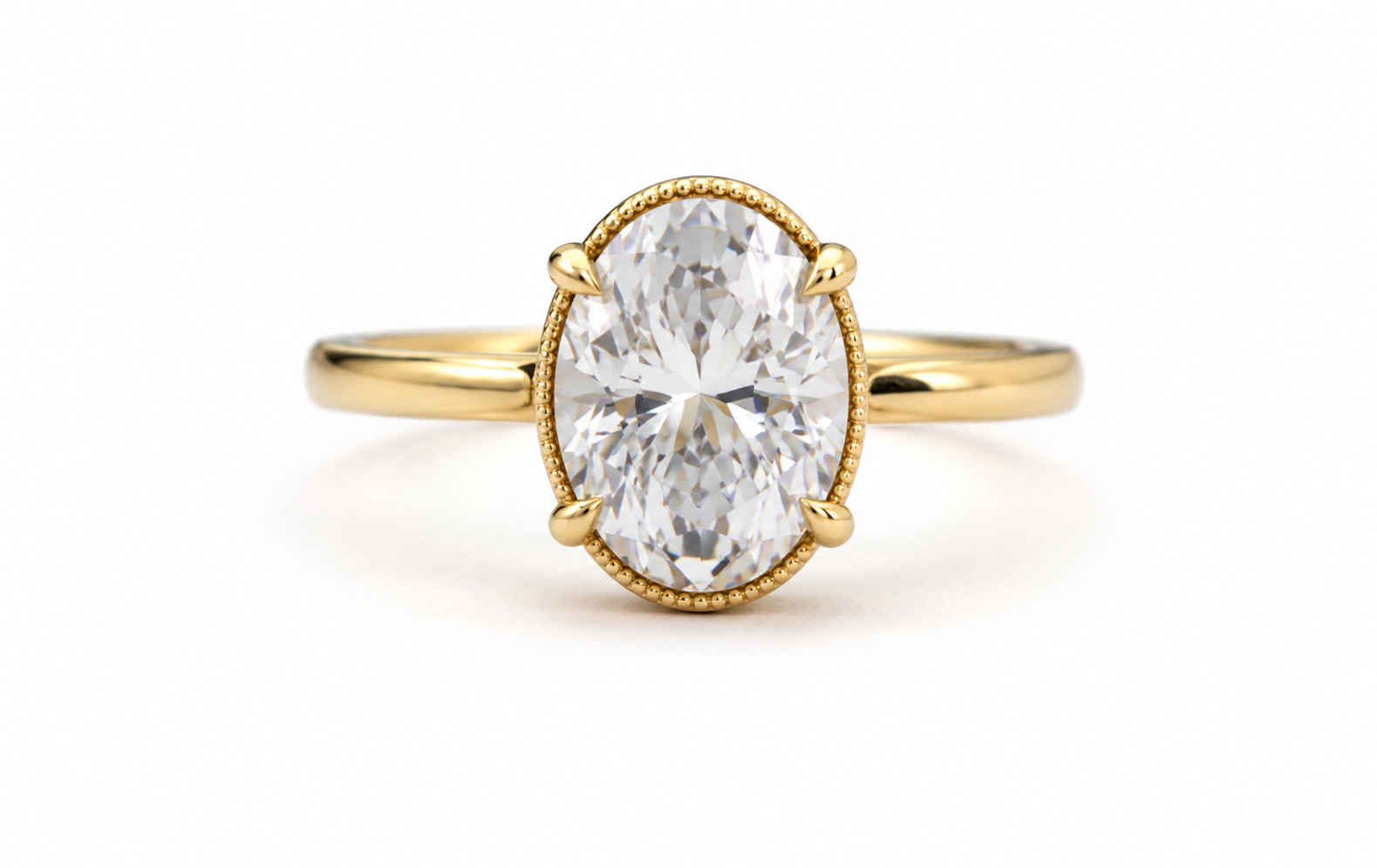 A yellow gold ring featuring an oval-cut clear gemstone in a four-prong setting with a delicate beaded border, shown on a plain white background.