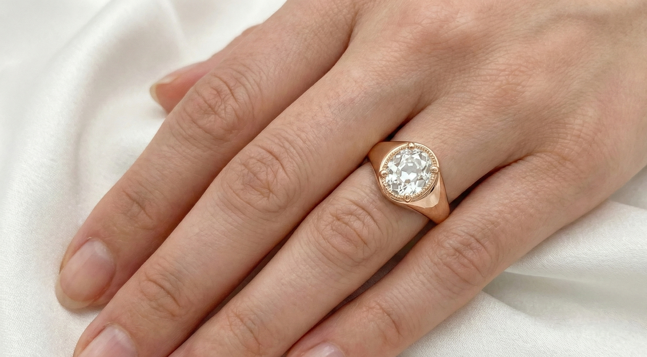 Rose gold ring with a diamond on a hand against a white background